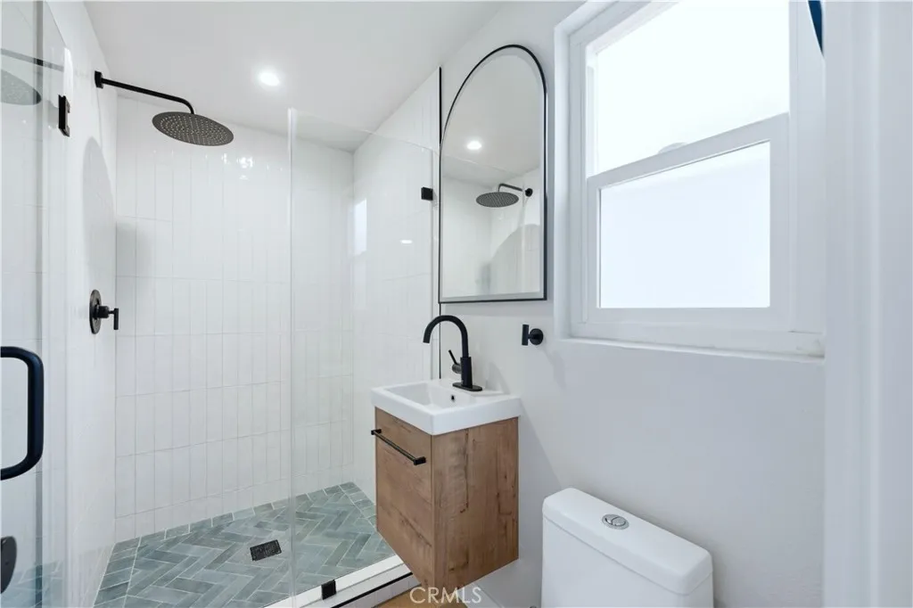 After: Renovated bathroom with custom tiled shower, glass enclosure, wood vanity and matte black fixtures