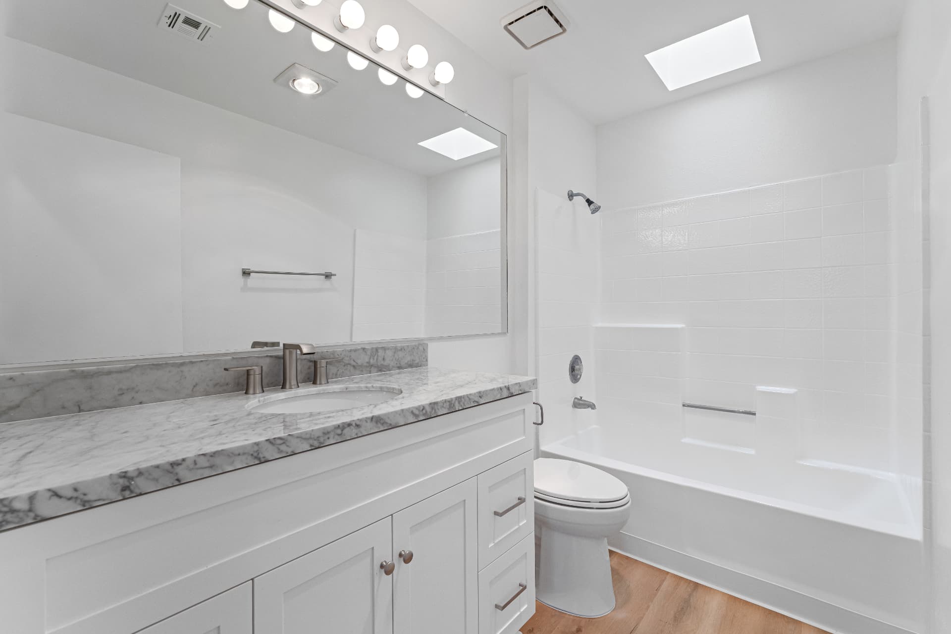 After: Renovated bathroom with white shaker vanity, marble counter, new fixtures and tub surround