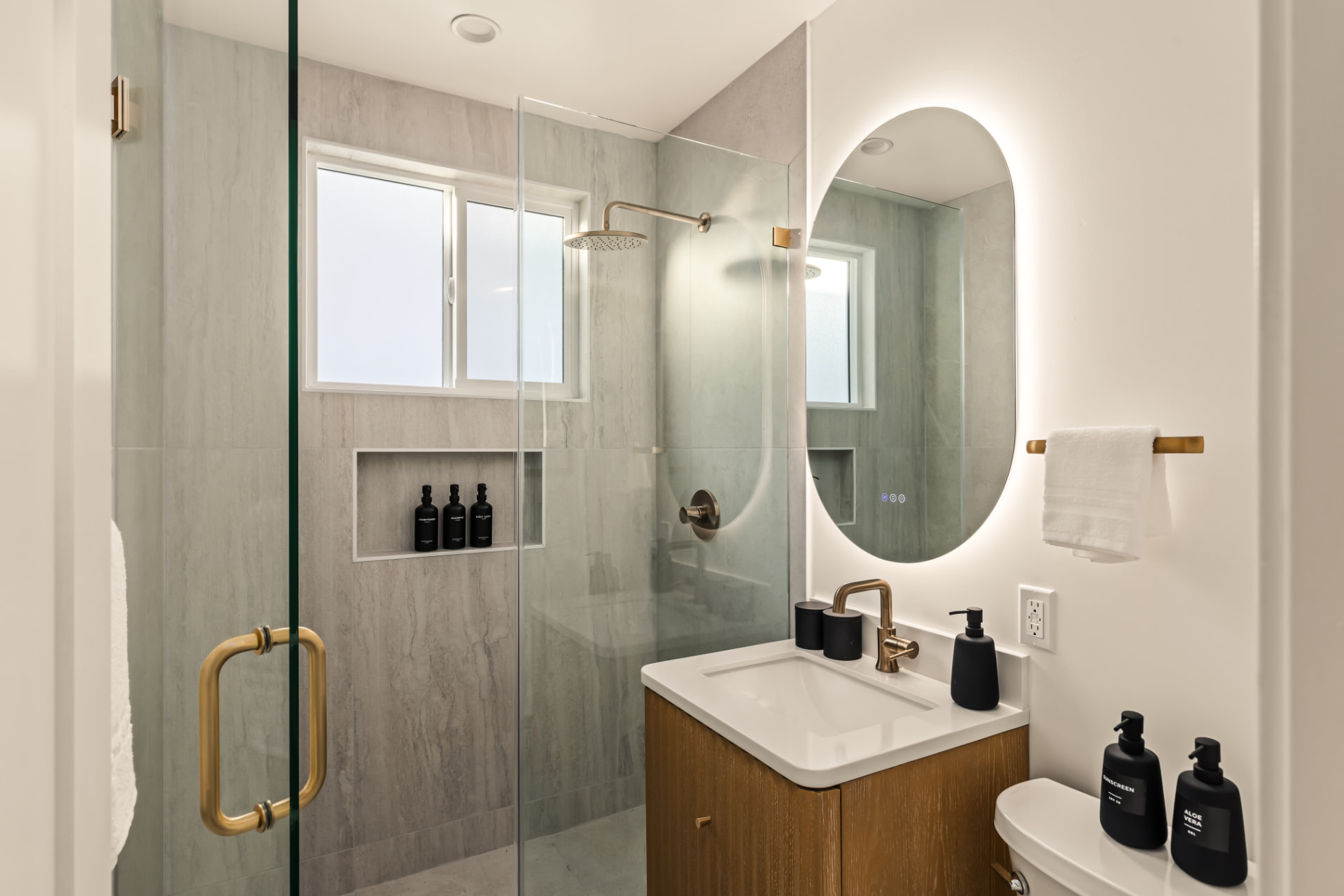 After: Renovated bathroom with glass shower, tiled walls and backlit mirror