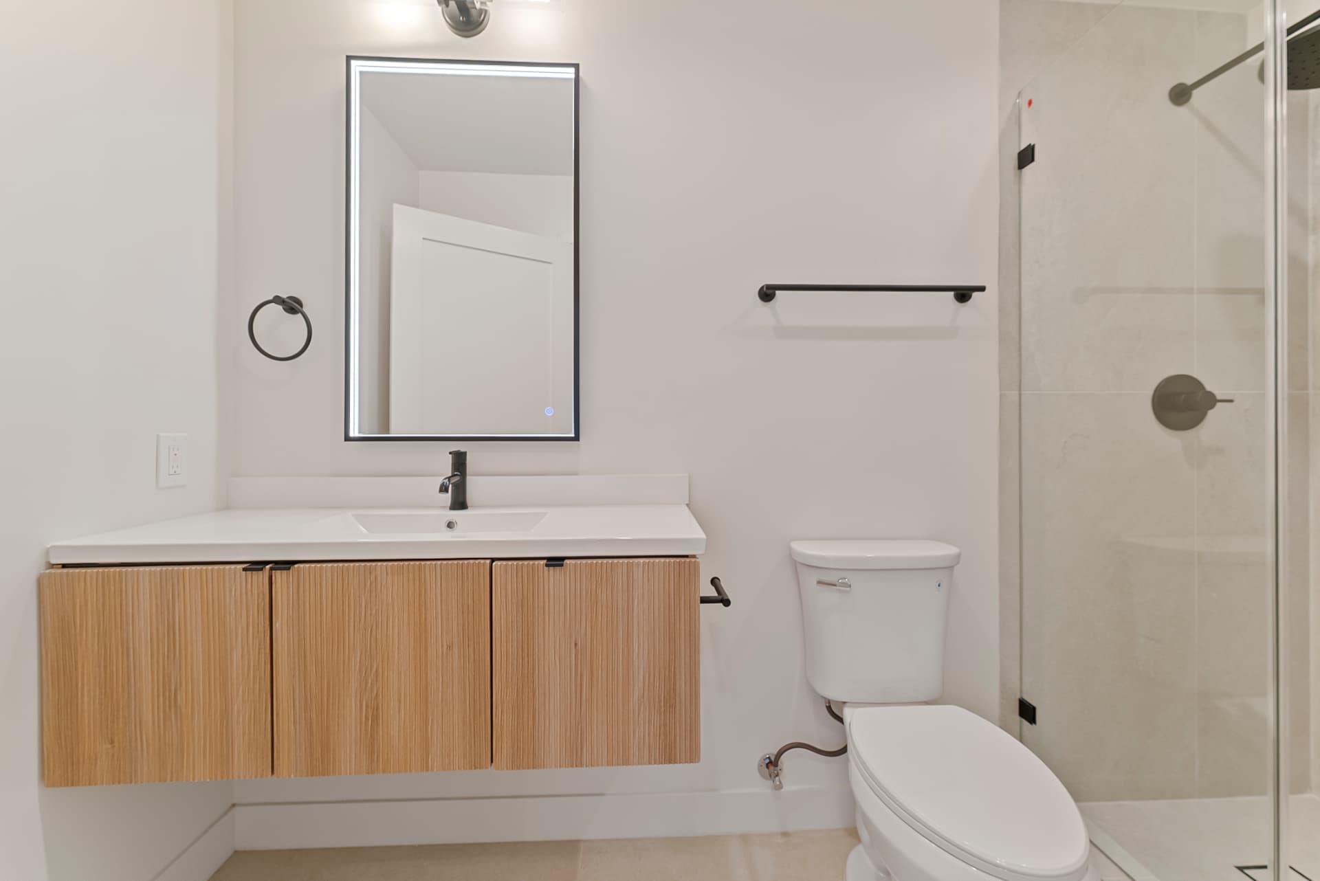 After: Renovated bathroom with floating wood vanity, backlit mirror and glass walk-in shower