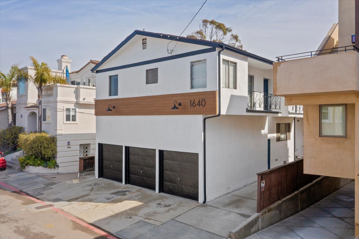 After: Renovated front of the building with new white stucco, wood accent panel and new garage doors