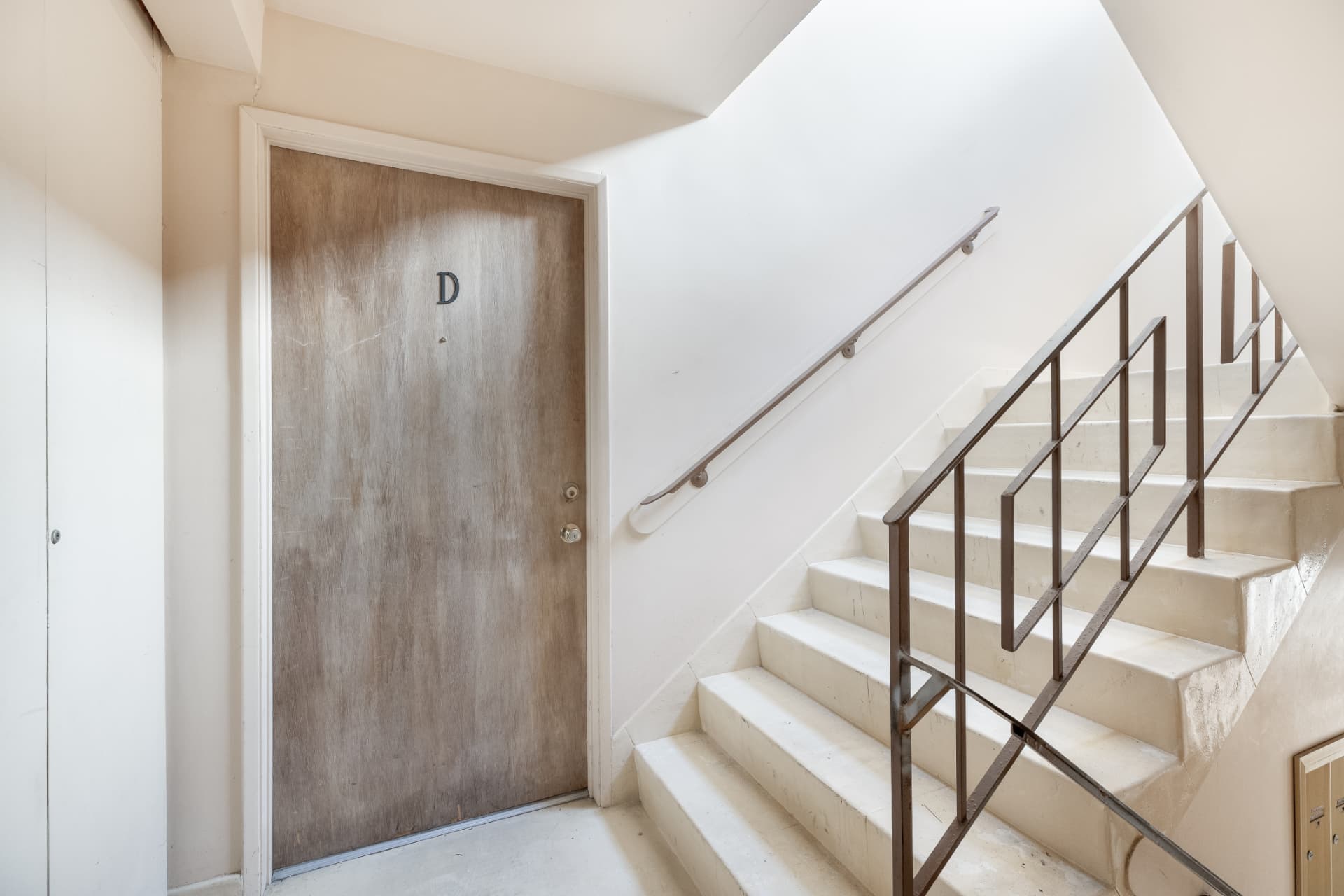 Before: Common hallway and staircase before renovation with worn entry door and older railing