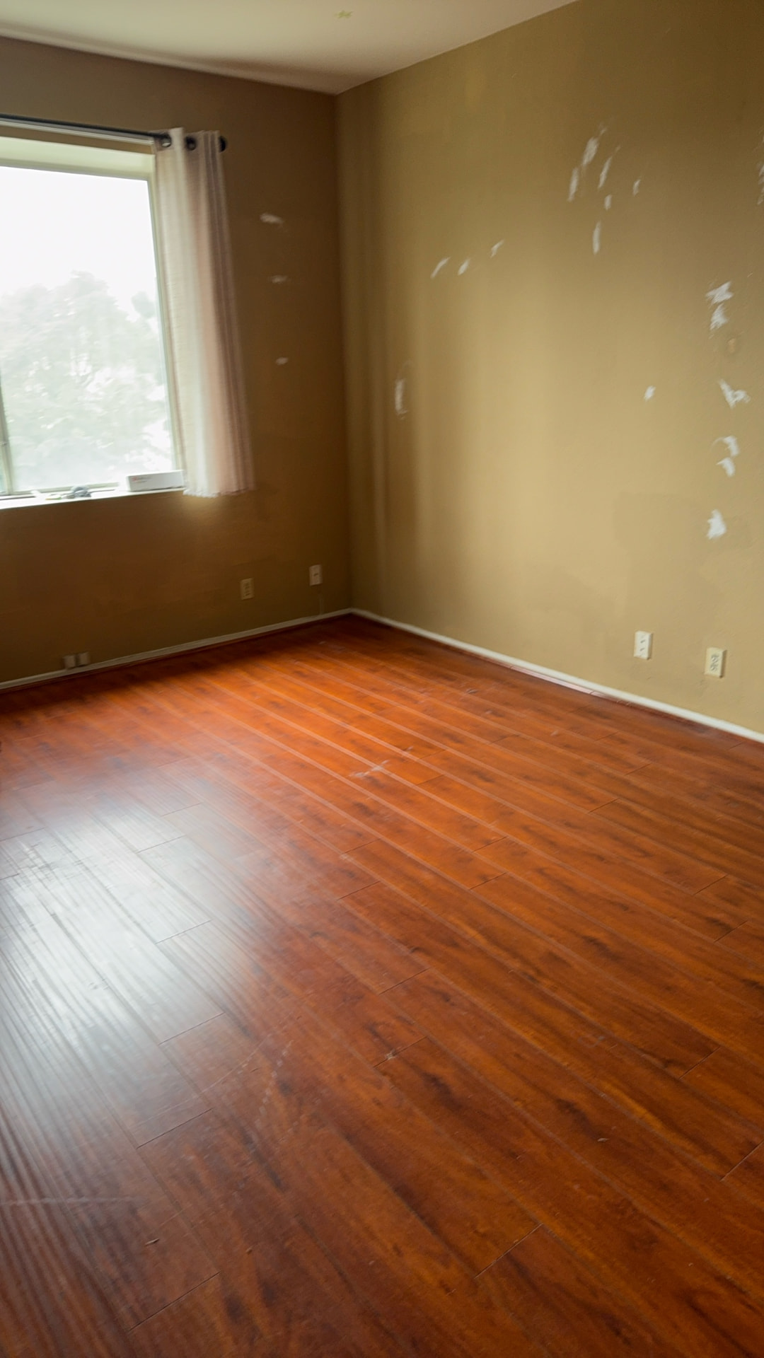 Before: Bedroom before renovation with worn walls and orange laminate flooring