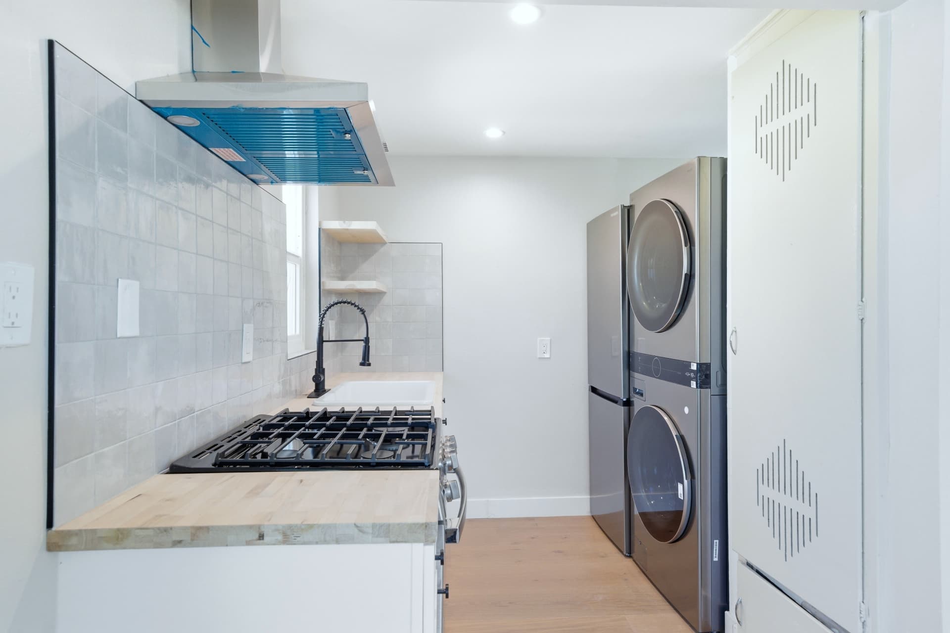 After: Renovated kitchen with white shaker cabinetry, butcher block counters, tile backsplash and in-unit washer and dryer