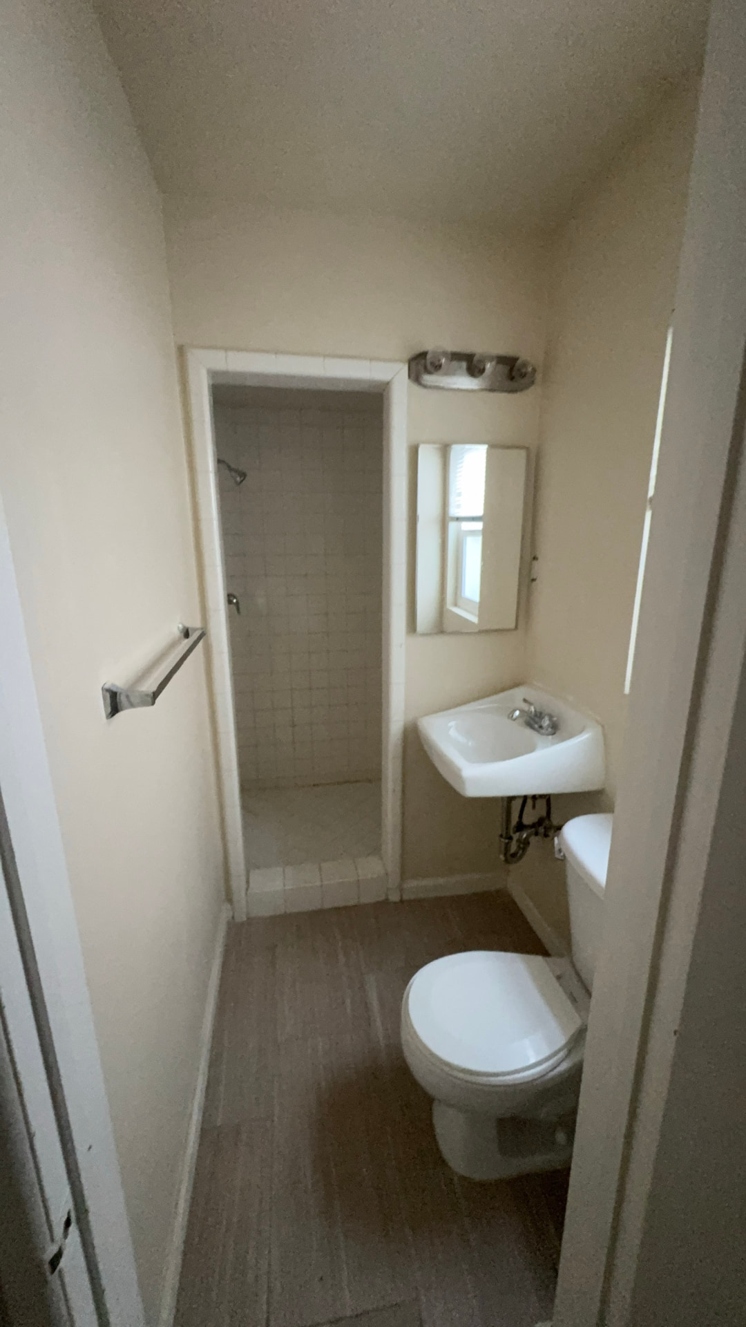 Before: Bathroom before renovation with tiled shower stall and wall-hung sink