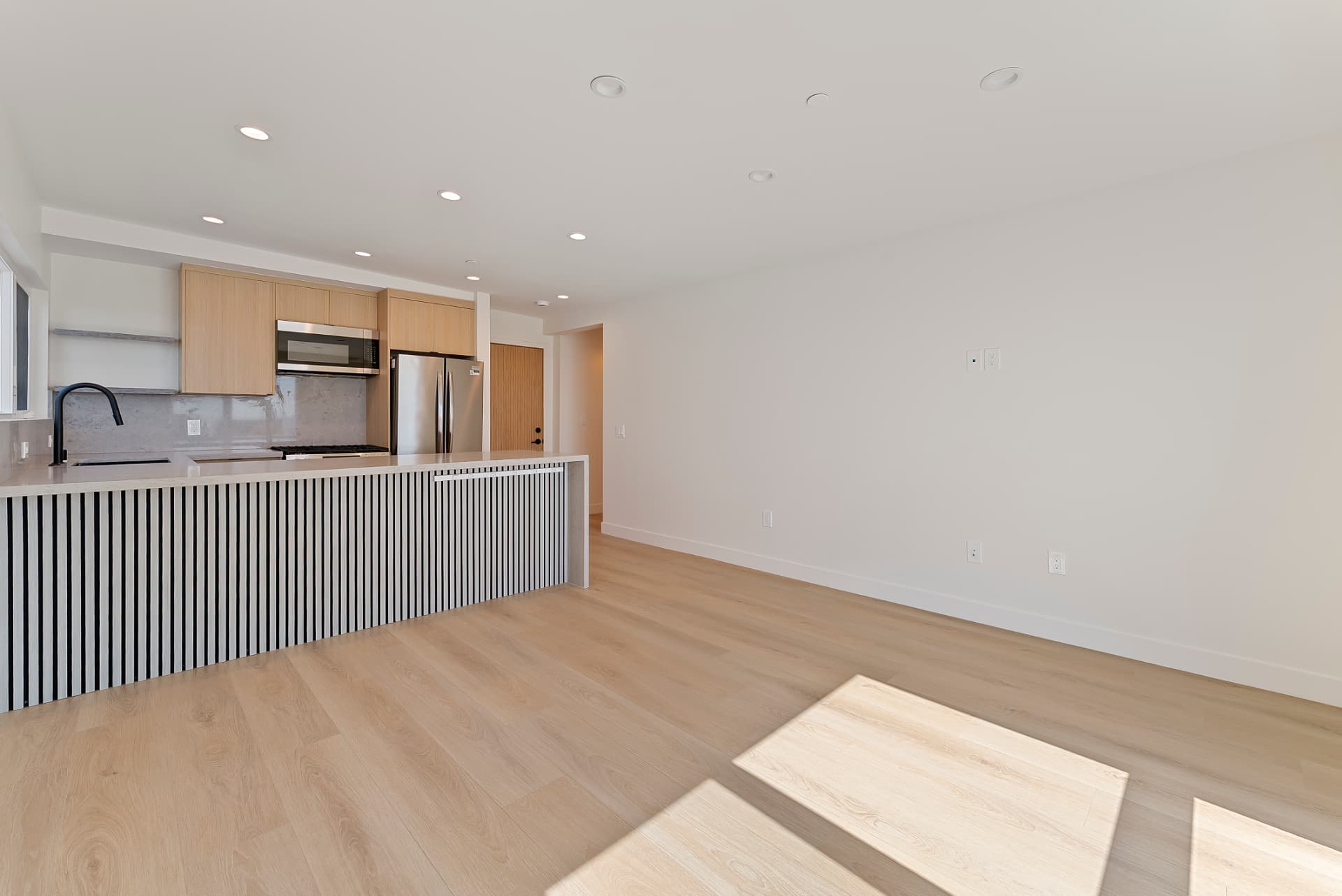 After: Renovated open kitchen and living area with light wood flooring, island and stainless appliances